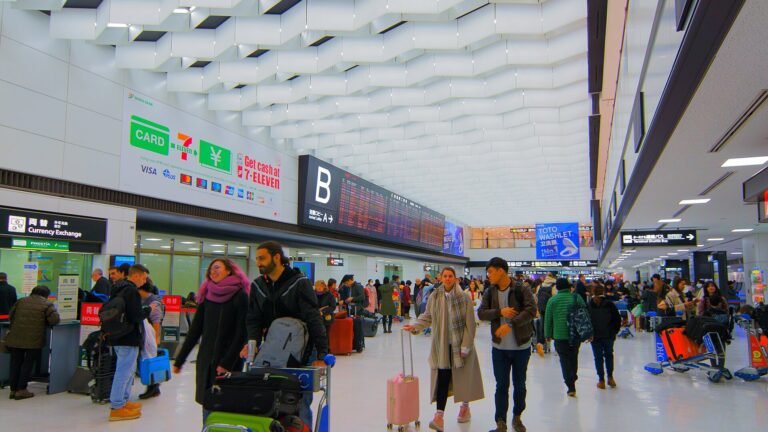 Travelers with suitcases walking through the arrivals lobby of Narita Airport Terminal 2 under a white ceiling