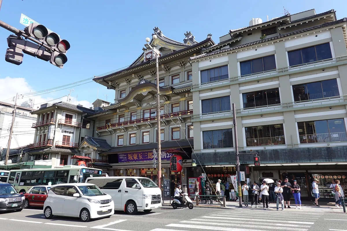 A traditional building with an ornate facade beside modern buildings on a street with cars, a traffic light, and pedestrians
