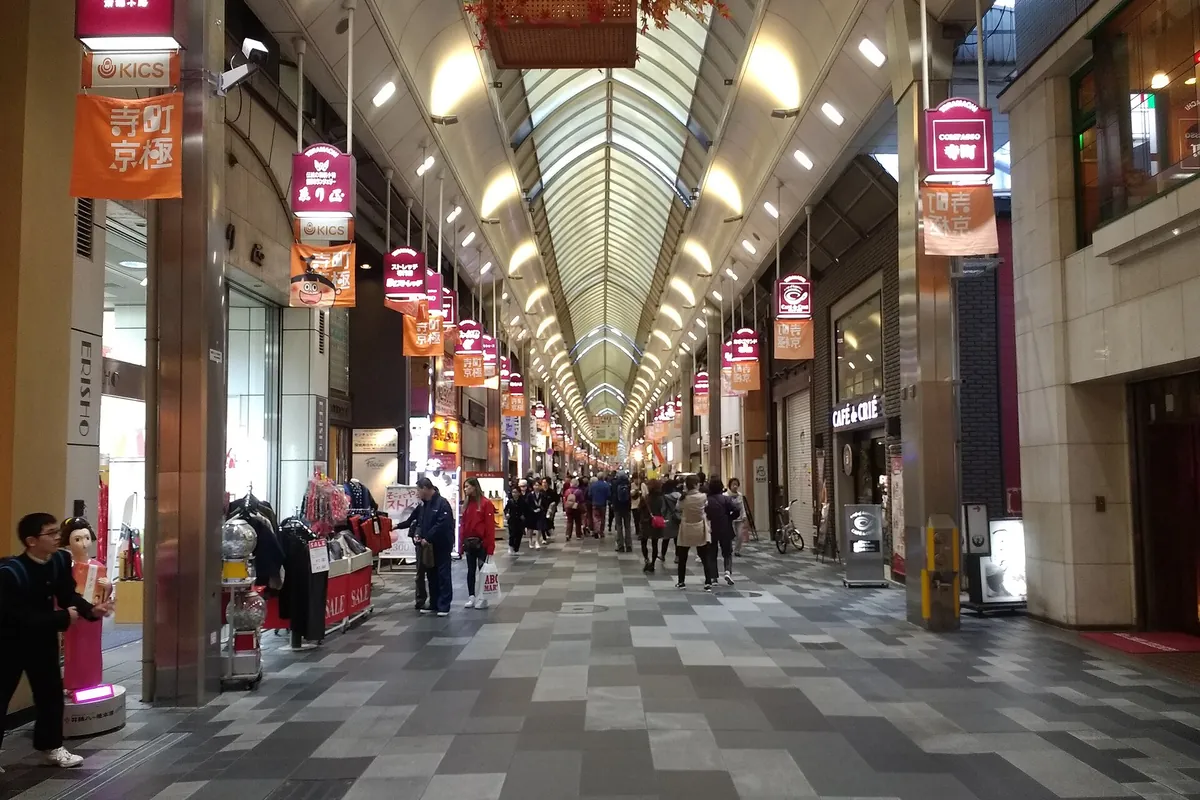 A covered shopping arcade lined with shops and hanging banners, with people walking on Teramachi Street in Kyoto