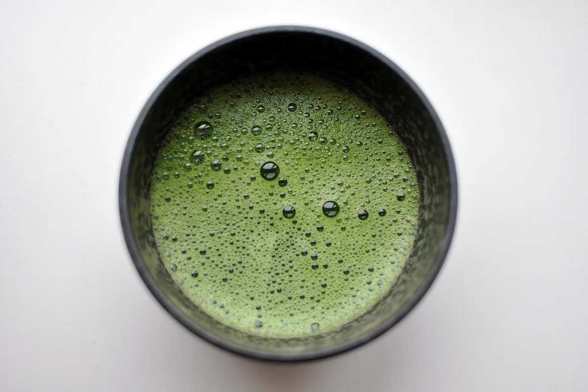 Whisked matcha with a frothy, bubbly surface in a dark bowl on a white background