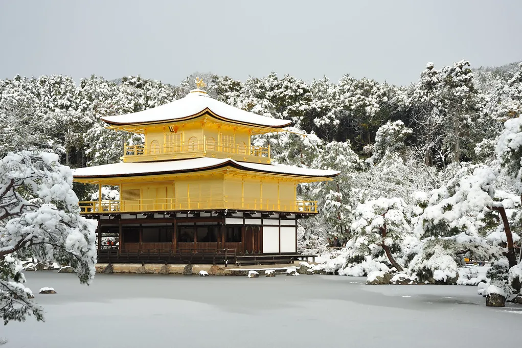 Kinkaku-ji golden pavilion in Kyoto covered in snow, reflected in a pond surrounded by snow-covered trees